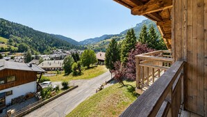 Un balcón de madera con vistas a un pueblo, casas y montañas al fondo.