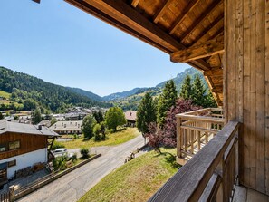 Un balcon en bois donnant sur une ville, avec des maisons et des montagnes en arrière-plan.