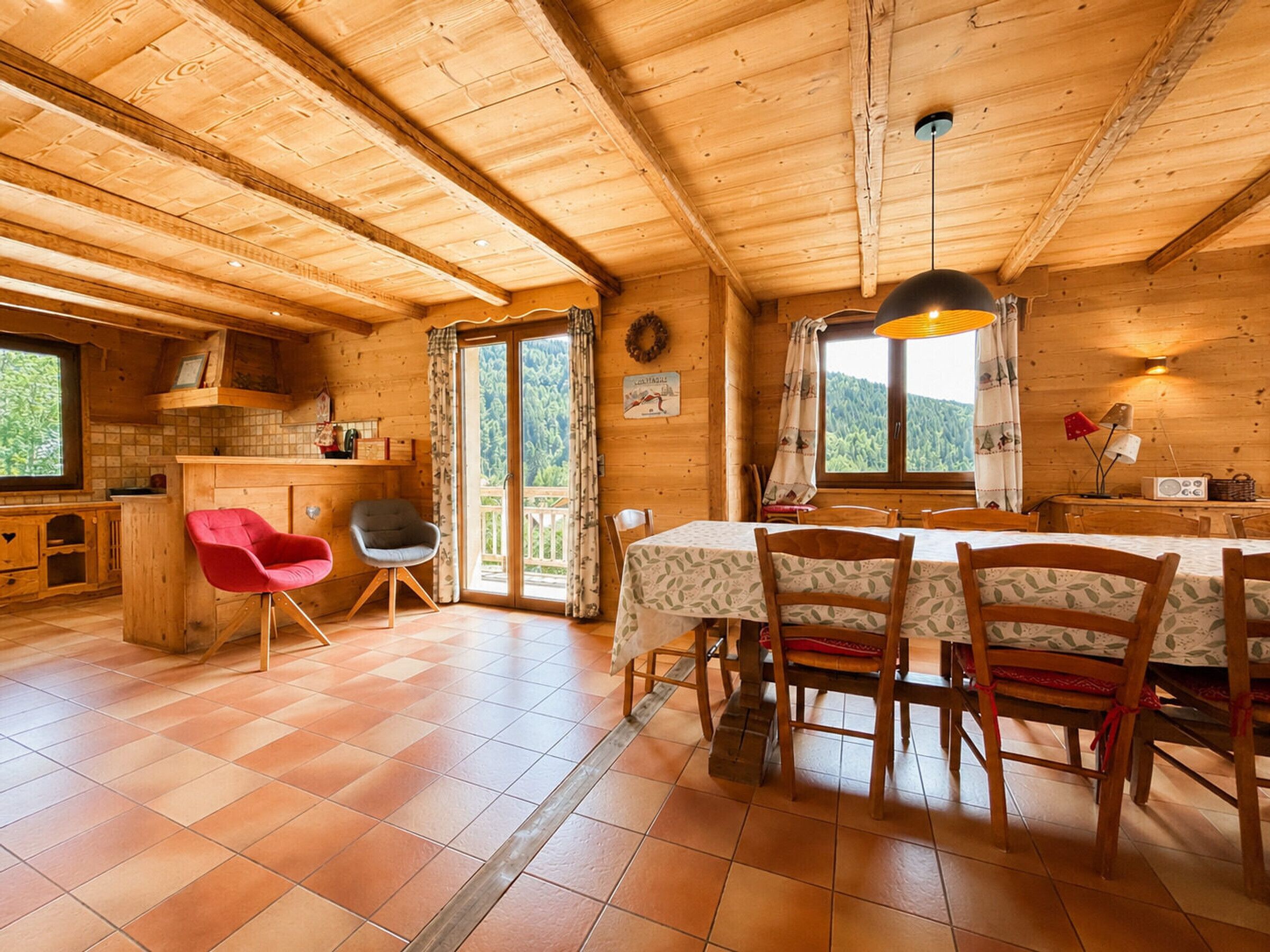 Interior de una cabaña de madera con comedor, cocina y un amplio ventanal con vistas.