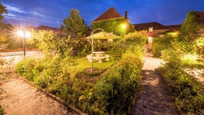 A well-lit garden area with a table and chairs, surrounded by lush greenery and a pathway. - Aux Charmes de Maintenon - Adults Only (Maintenon)