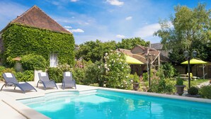 A swimming pool with lounge chairs, surrounded by greenery and a building with a tiled roof. - Aux Charmes de Maintenon - Adults Only (Maintenon)