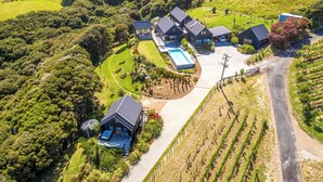 An aerial view of a large estate with multiple buildings, a swimming pool, and vineyard rows. - Te Whau Retreat - Guest House (Waiheke Island)