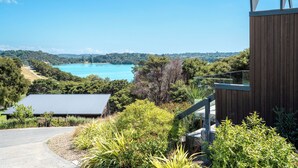 A modern building with a metal roof, surrounded by lush greenery and a view of a turquoise lake. - Te Whau Retreat - Guest House (Waiheke Island)