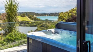 A hot tub with a scenic ocean view, surrounded by lush greenery and a wooden deck. - Te Whau Retreat - Guest House (Waiheke Island)