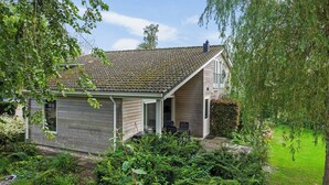 Una casa con garage coperto, tetto a falde e giardino con diverse piante e arbusti.