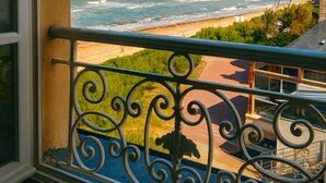 Ein Balkon mit schmiedeeisernem Geländer, der auf einen Strand und das Meer blickt.
