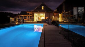 Ett modernt hus med en swimmingpool, stora fönster och en väl upplyst interiör.