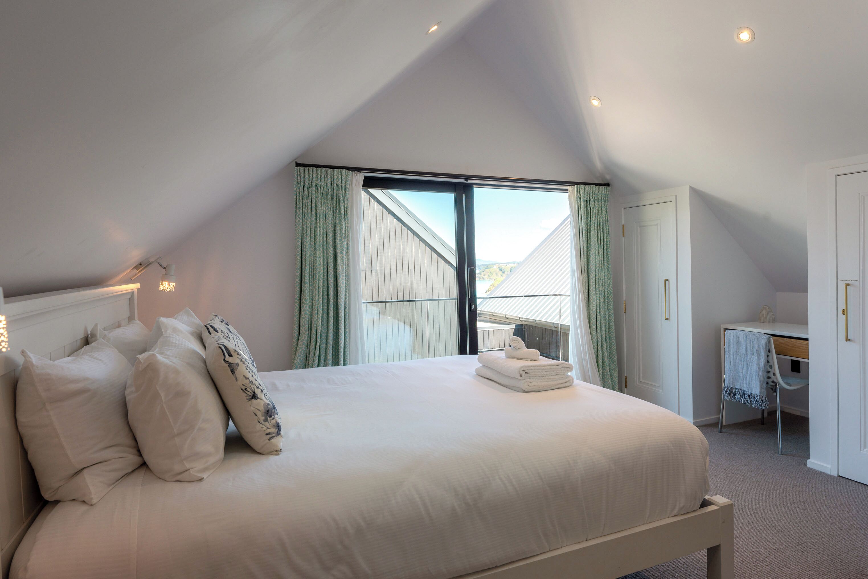 A bedroom with a large bed, a desk, and a view of the outdoors.