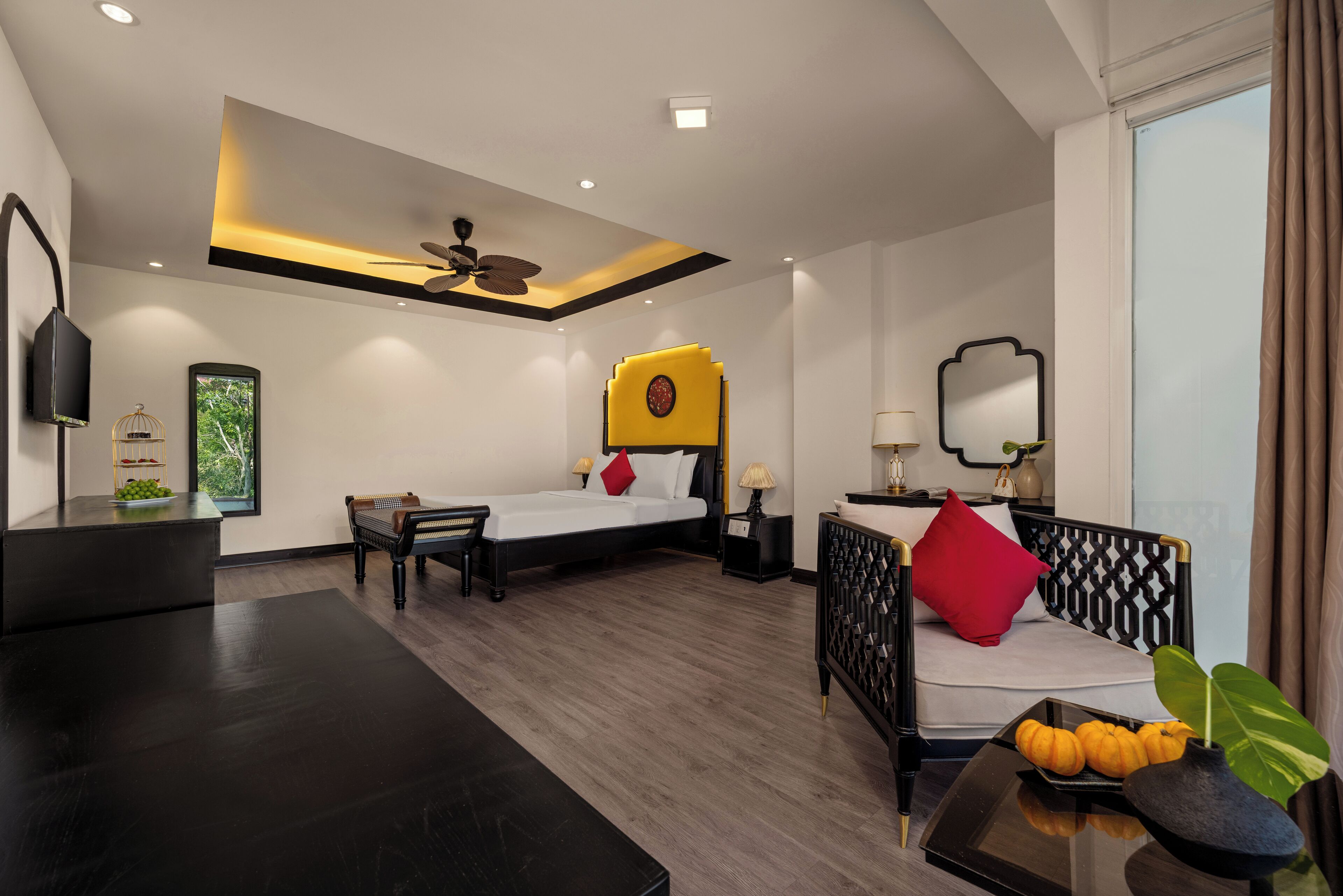 A modern hotel room with a bed, a sofa, a desk, and a ceiling fan.