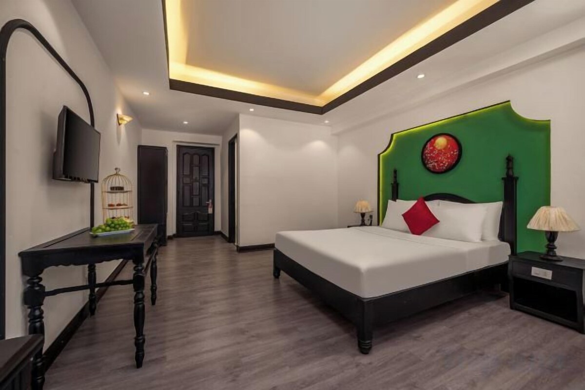 A hotel room with a bed, bedside table, lamp, and a television on the wall.