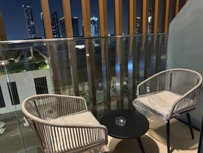 A balcony with two wicker chairs and a small round table, overlooking a cityscape at night. - VESTA - Dubai Residence (Dubai)