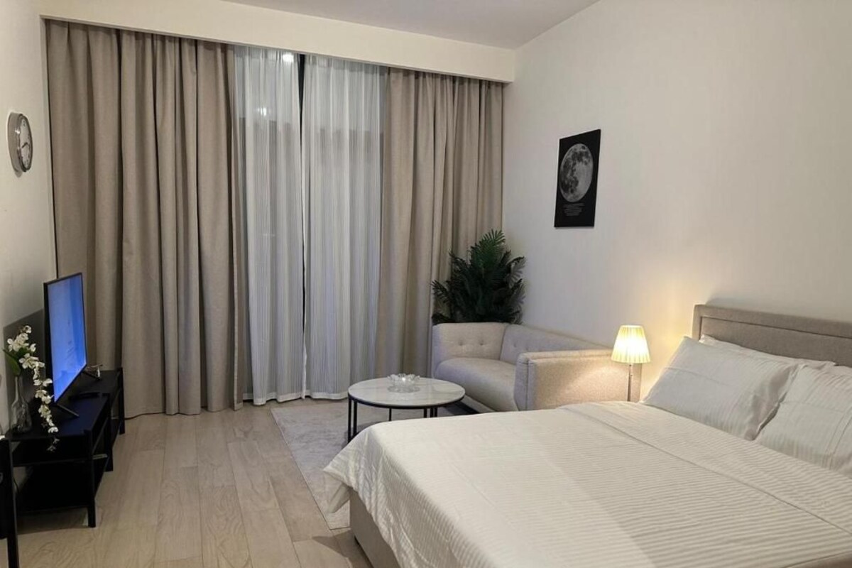 A hotel room with a bed, a sofa, a small table, a TV, and curtains.
