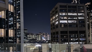 Un paisaje urbano nocturno con edificios modernos, cielo despejado y un planeta distante visible.