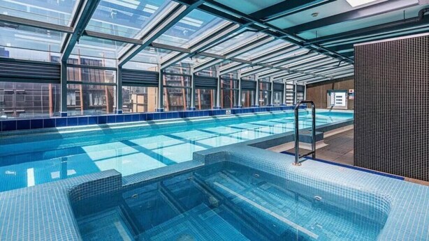 Una amplia piscina interior con techos de vidrio transparente y bordes azulejados en azul.