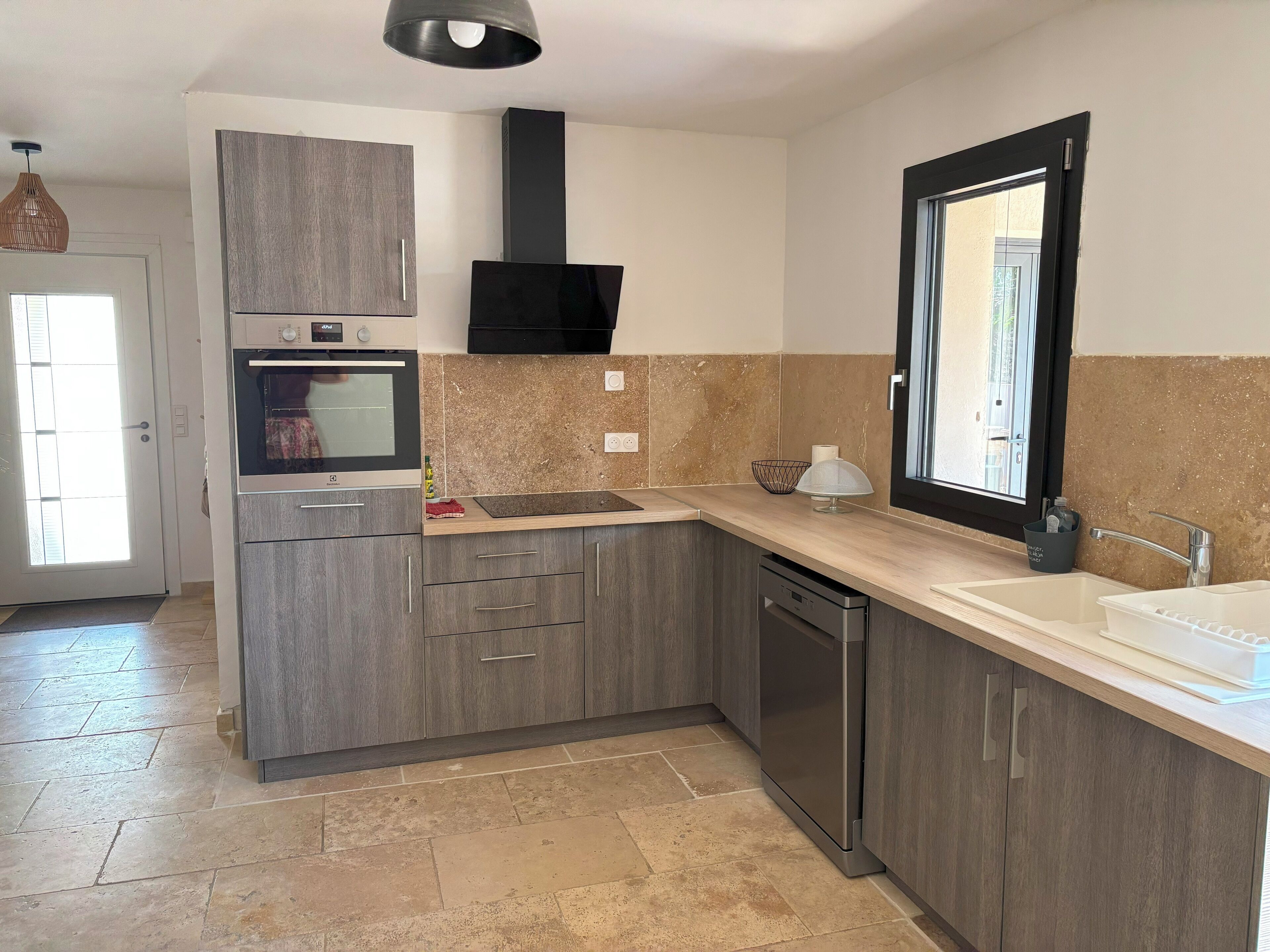 Una cucina moderna con mobili grigi, forno integrato, lavastoviglie e una finestra con vista.
