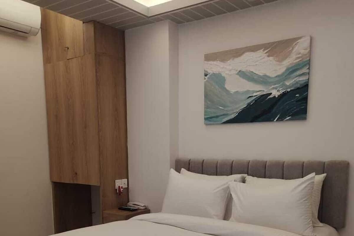 A bedroom with a bed, a nightstand, a painting, and a wooden wardrobe.