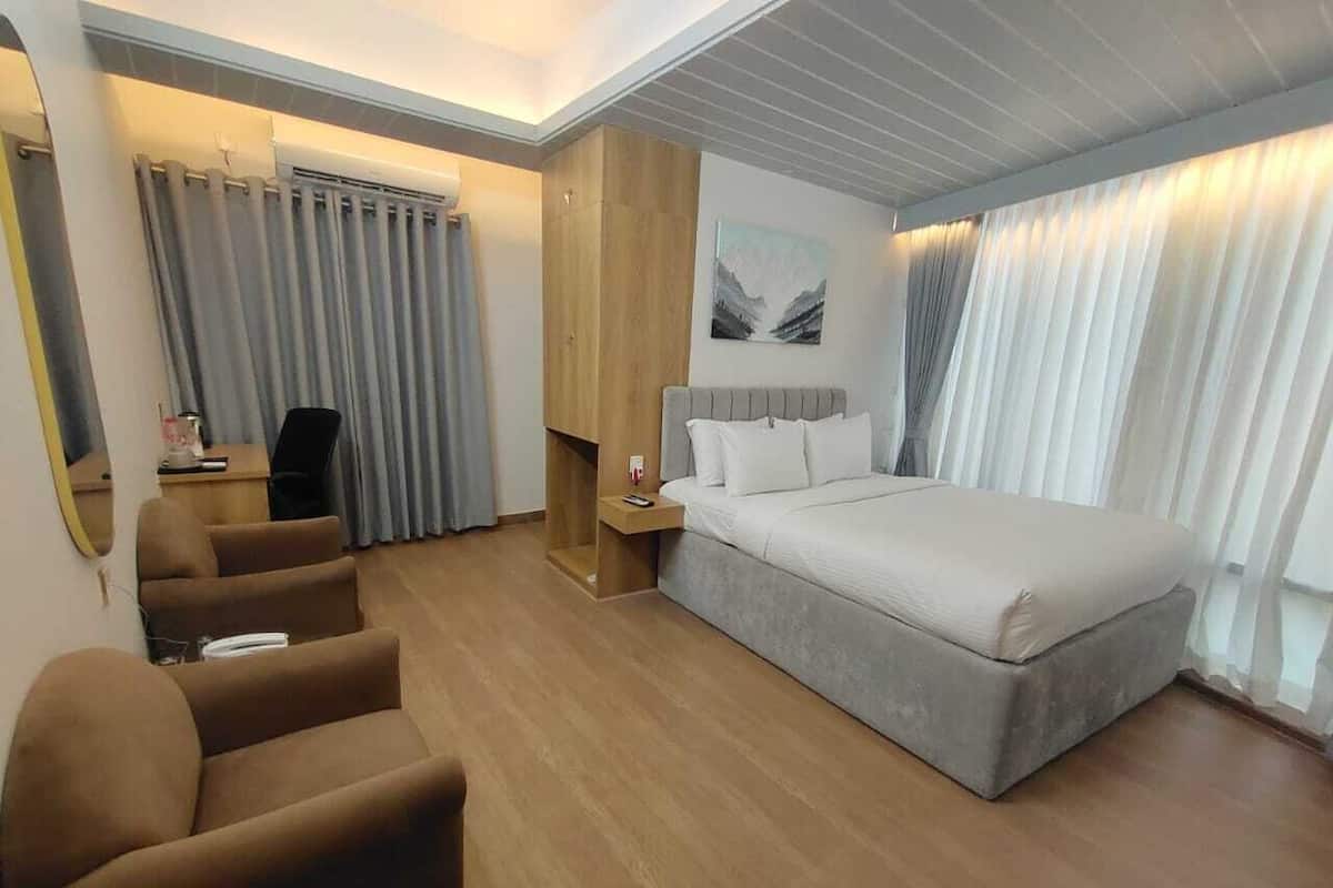 A modern hotel room with a large bed, a seating area with chairs, a desk, and a large mirror.