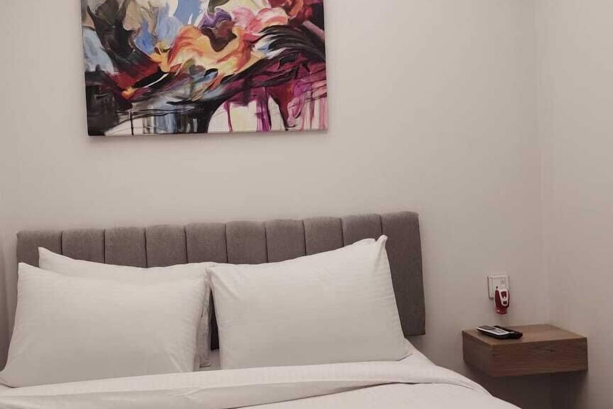 A modern bedroom with a large bed, a grey headboard, and a colorful abstract painting on the wall.
