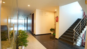 A modern hotel lobby with a glass wall, a staircase, and potted plants. - Hotel Royal Stay inn (Patancheruvu)