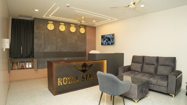 A reception area with a reception desk, a grey sofa, a small table, and a ceiling fan. - Hotel Royal Stay inn (Patancheruvu)