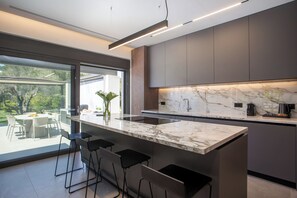 Una cocina moderna con encimera de mármol, taburetes de bar y vistas al exterior.