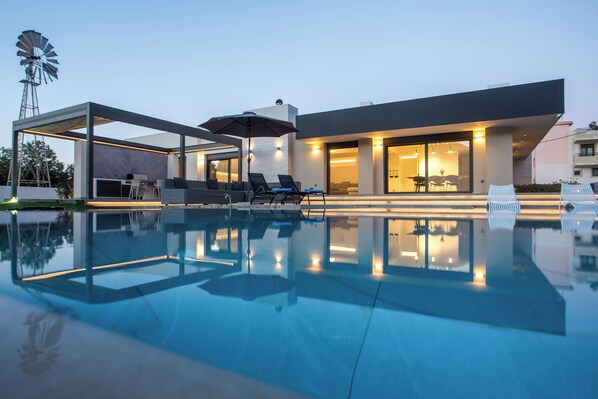Una casa moderna con piscina, mobiliario exterior y un molino.