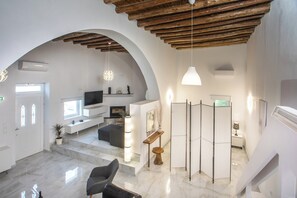 A modern interior with a high ceiling, arched doorways, a flat-screen TV, a seating area, and a staircase.