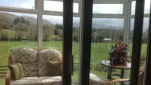 Ein Wintergarten mit einer Couch und Sesseln, große Fenster mit Blick auf eine grüne Landschaft.