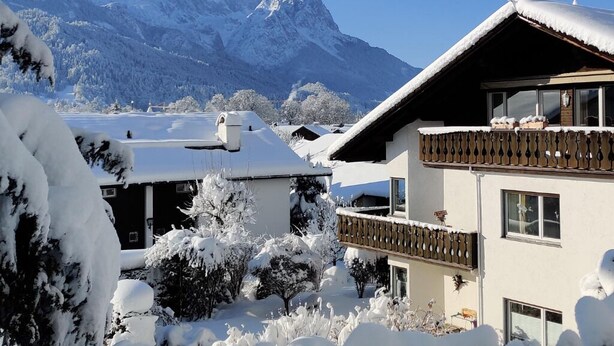 A snow-covered building with a balcony, surrounded by trees and mountains in the background. - AlpenHorizont: Spacious vacation apartment with a dream view for families & friends (Garmisch-Partenkirchen)