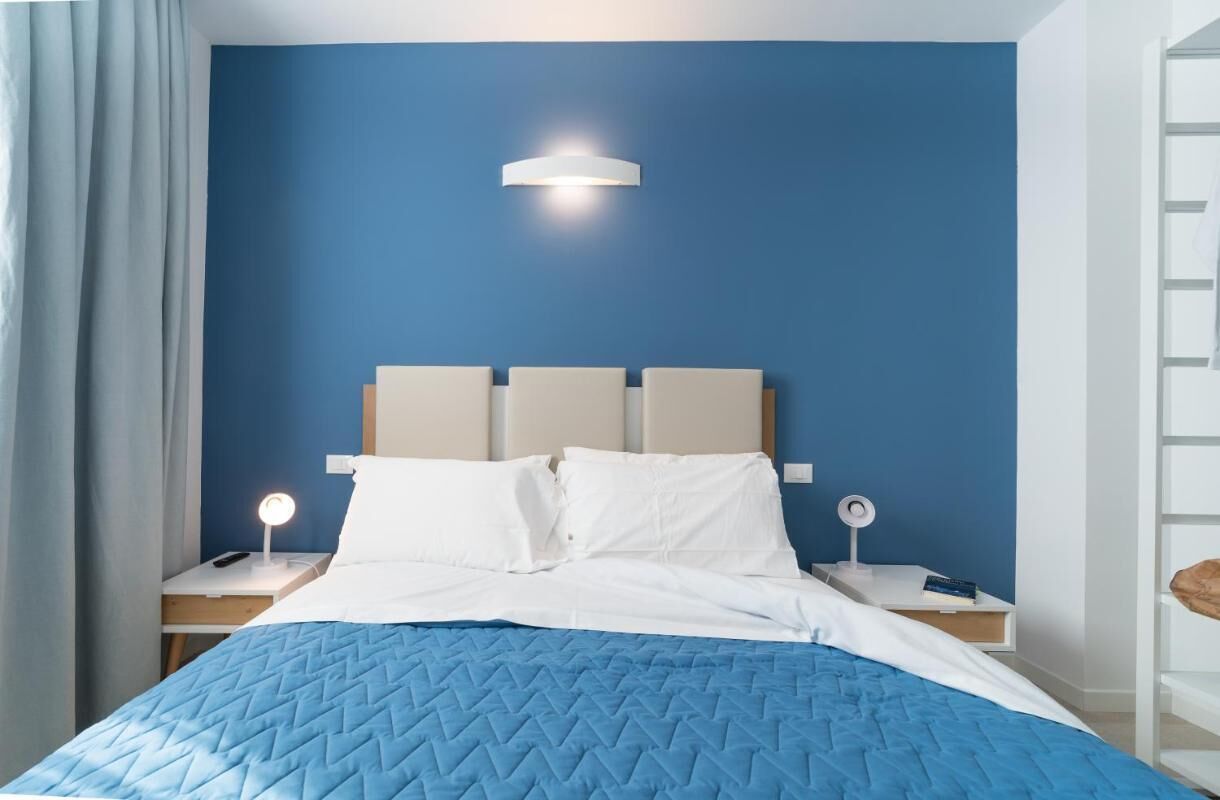 Una habitación de hotel con cama, mesita de noche, lámpara y una lámpara fijada a la pared.