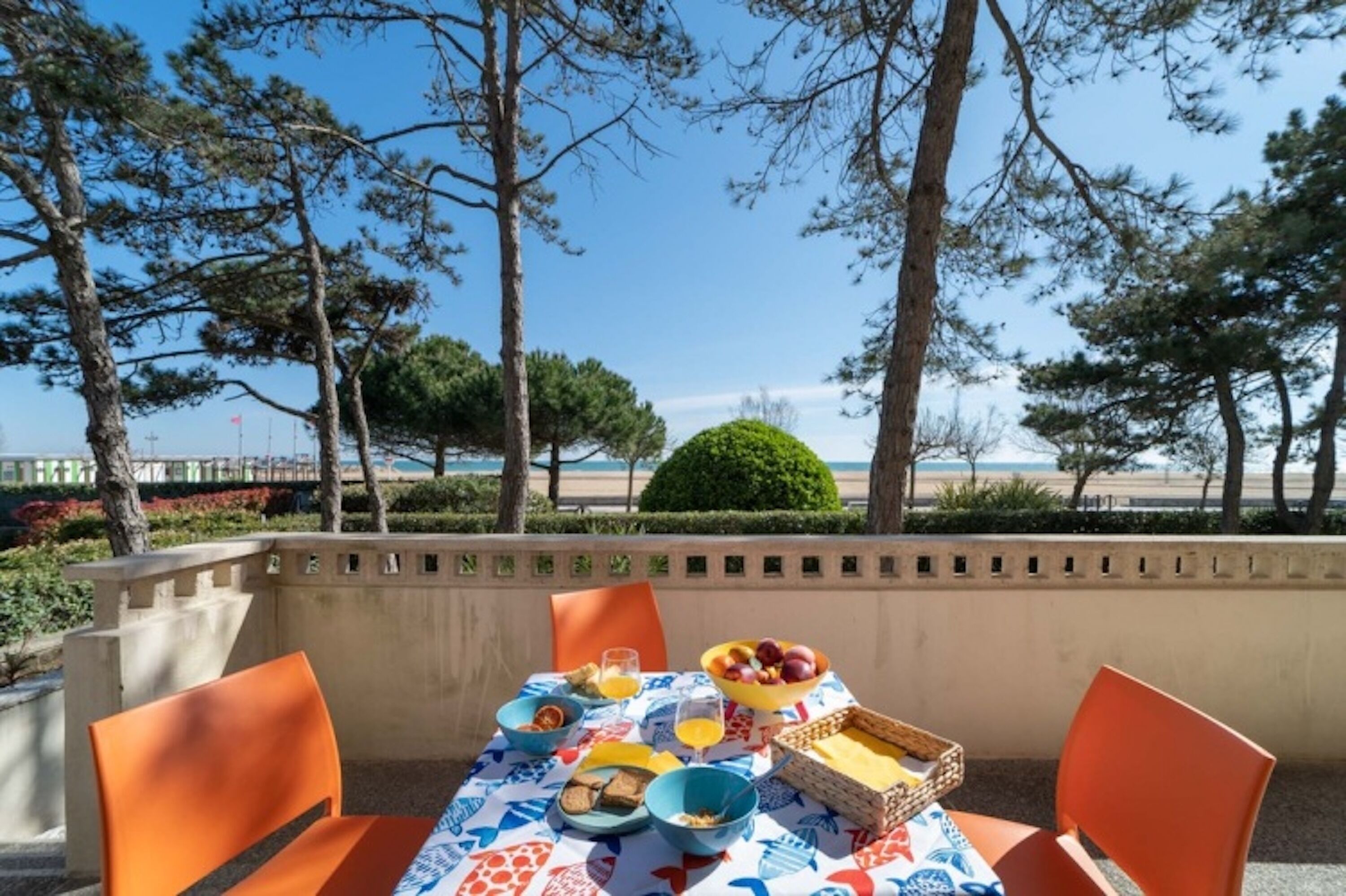 An outdoor dining area with a table set for breakfast, overlooking a beach and trees.