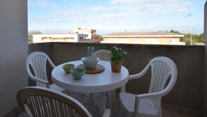 A balcony with a round table and four white chairs, a potted plant, and a view of buildings in the background.