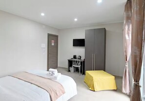 Una habitación de hotel con cama, escritorio, silla, televisor y armario.