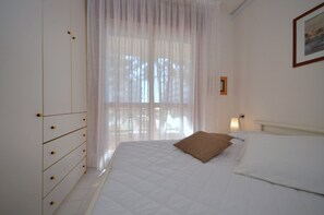 Une chambre à coucher comprenant un lit, une armoire, une fenêtre avec des rideaux légers et un luminaire fixé au mur.