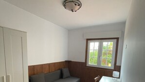 Ein gemütlicher Raum mit einer Sitzecke, einem kleinen Tisch, einem Kleiderschrank und einem Fenster mit Blick auf Grünflächen.