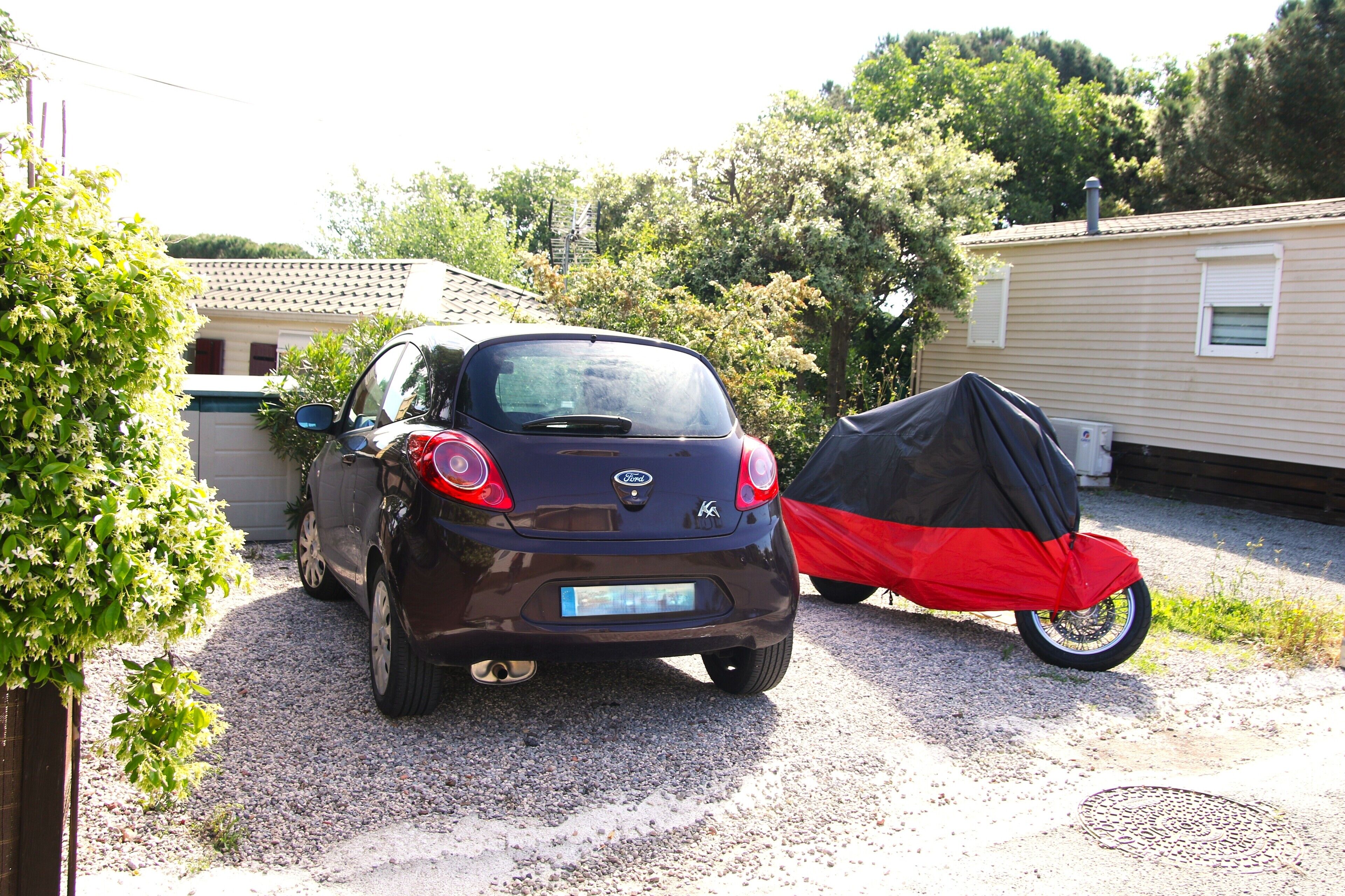 Un coche pequeño aparcado en una entrada de casa con una motocicleta cubierta cerca.