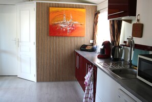 A modern kitchen with a wooden panel wall, a red kettle, a coffee maker, and a microwave. - Beautiful mobile home with a furnished patio, 7 km from the beach   (Puget-sur-Argens)