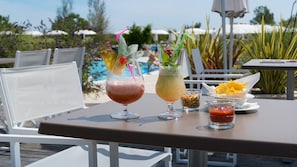 Una mesa con dos bebidas, un bol de nueces y un recipiente pequeño de salsa.