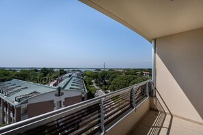 Un balcon offrant une vue sur un immeuble doté d’un toit végétalisé, entouré d’arbres et bordé par une étendue d’eau.