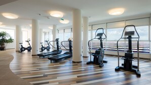 Un gimnasio con cintas de correr, bicicletas estáticas y máquinas elípticas, ventanas amplias y piso estampado.