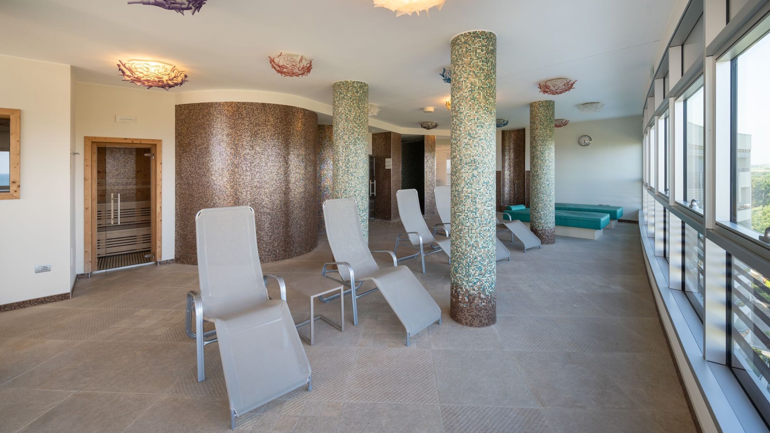 A modern waiting area with a row of chairs, a reception desk, and a large window offering a view.