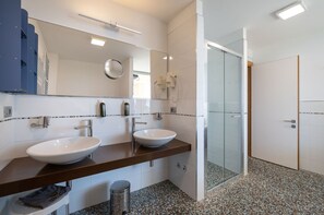 Ein modernes Badezimmer mit zwei Waschbecken, einem großen Spiegel und einer Duschkabine aus Glas.