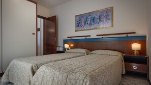 Ein Hotelzimmer mit zwei Betten, einem hölzernen Kopfteil, einem Gemälde, Nachttischlampen und einer Holztür.