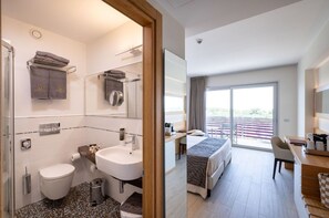 A modern hotel room with a bathroom, a balcony, and a desk area.