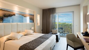 Ein Hotelzimmer mit einem großen Bett, einem Schreibtisch und einem Balkon mit Blick.