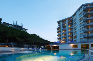 Un hotel con piscina, varios balcones y vistas a una colina.