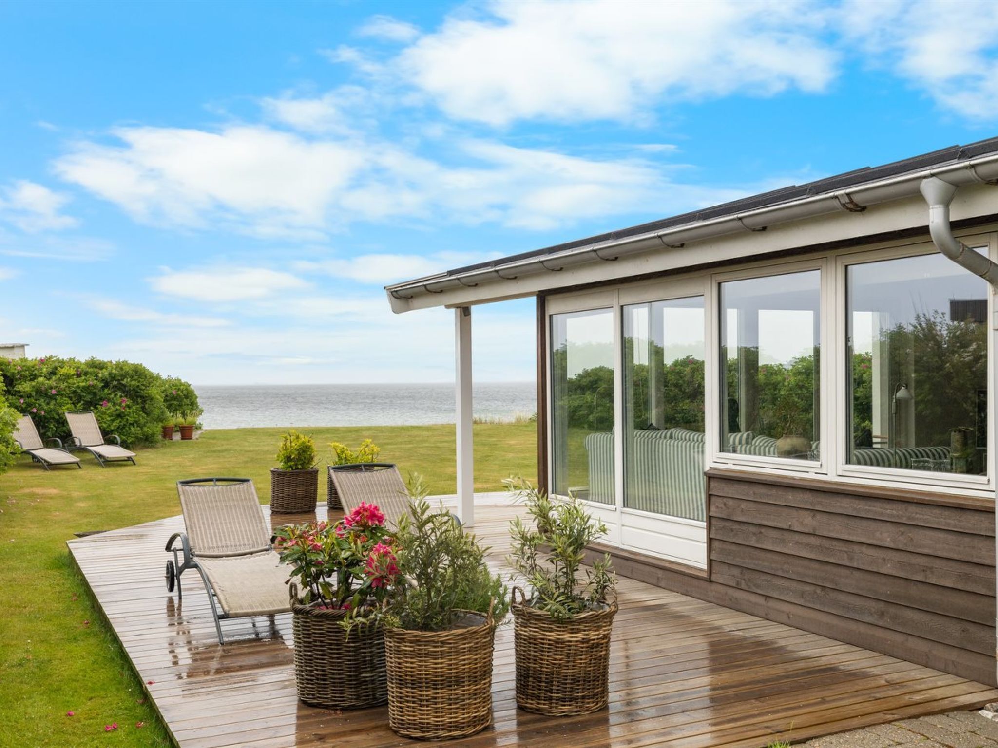 A wooden deck with wicker planters, lounge chairs, and a view of the sea.