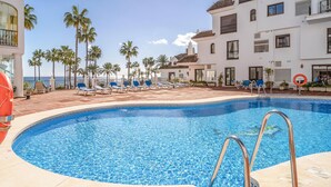 A swimming pool with lounge chairs, palm trees, and a building with balconies.