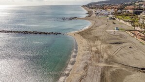 A coastal beach with a rocky breakwater, a sandy shore, and a town in the background.