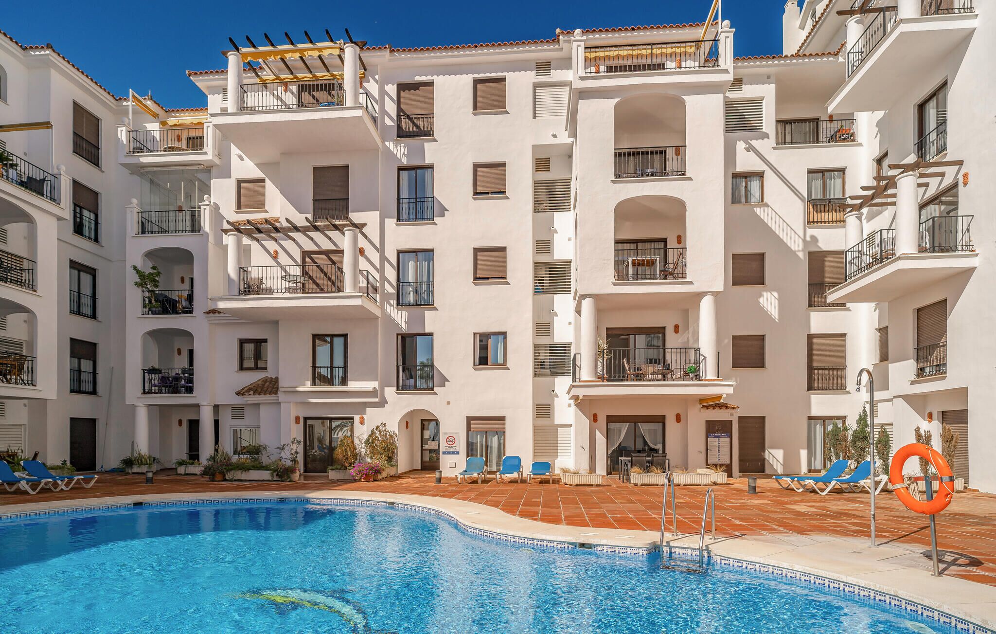 A multi-story hotel with balconies, a swimming pool, and outdoor seating areas.